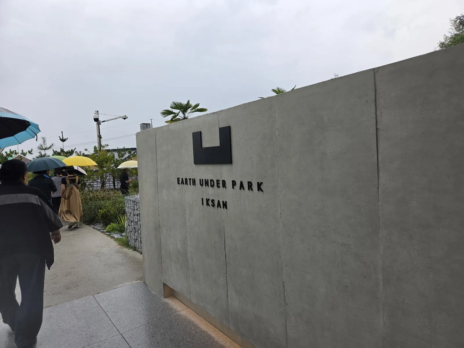 입구 벽의 EARTH UNDER PARK IKSAN, 우산 쓰고 들어가는 사람들