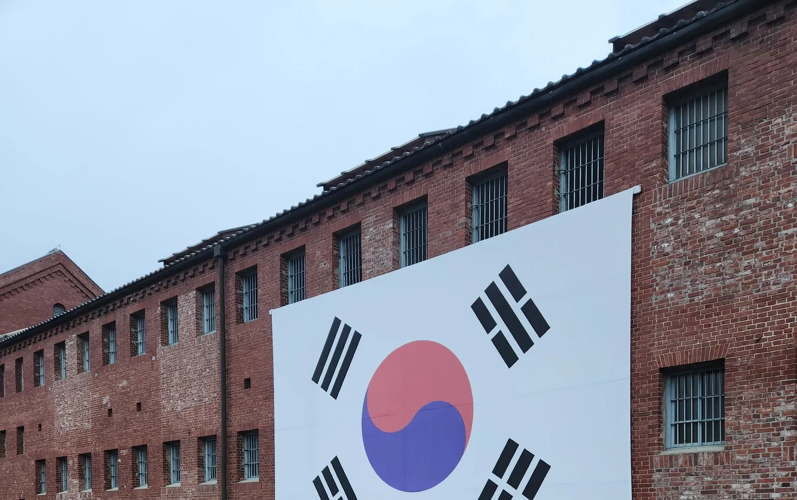 2025년 3월 1일 18:02 — 흐린 하늘 아래 붉은 벽돌 옥사와 태극기