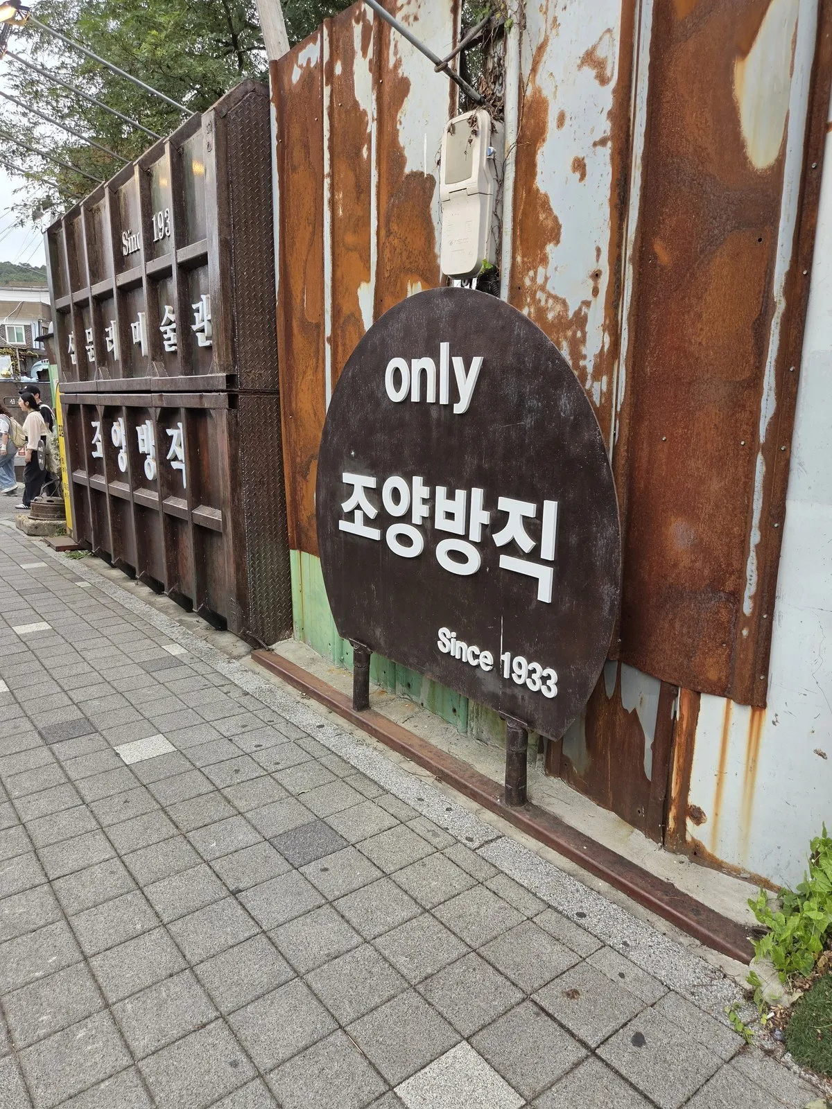 녹슨 철판 담장 앞의 'only 조양방직 Since 1933' 둥근 간판
