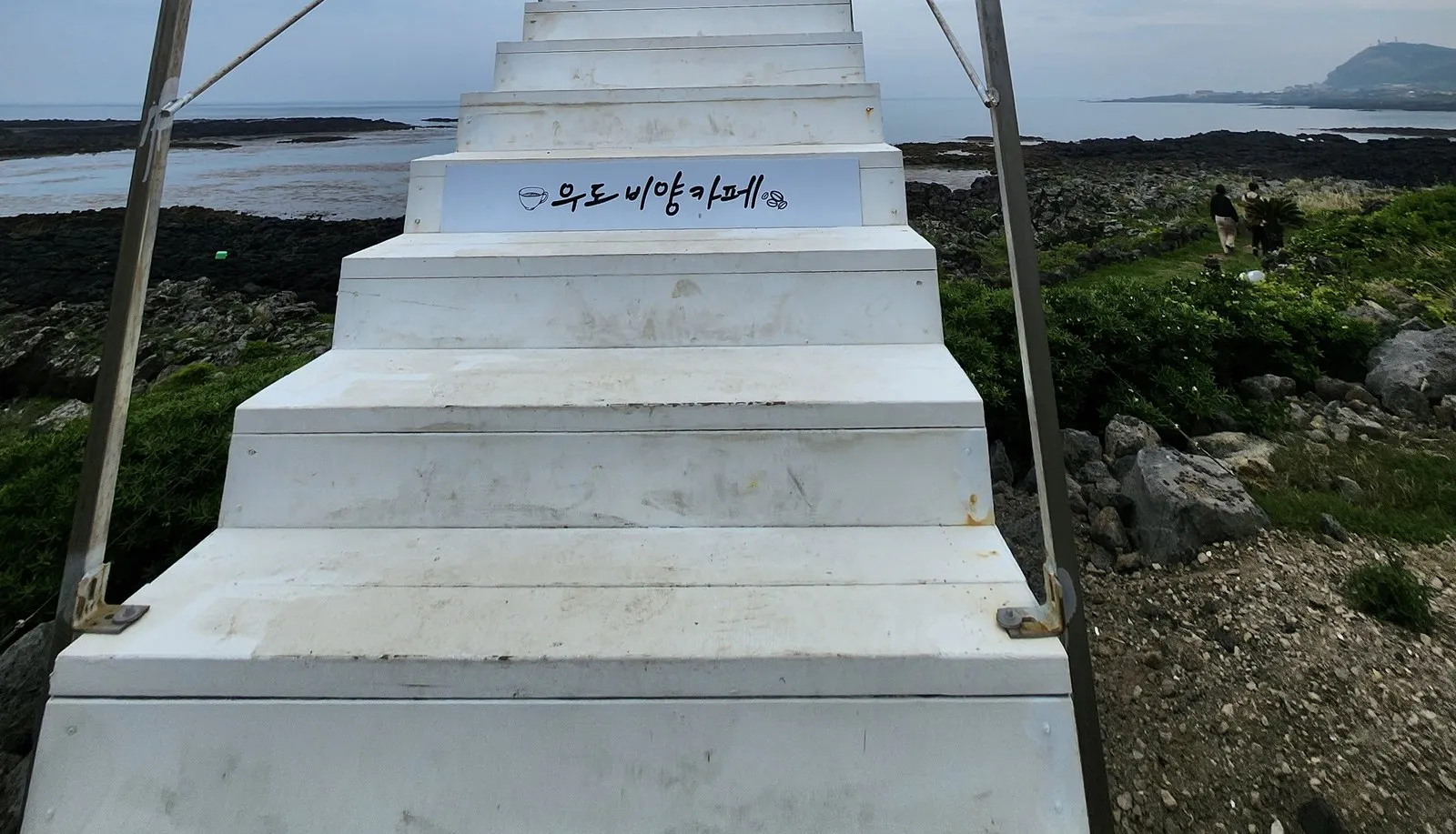 우도 — '우도 비양 카페'라고 적힌 흰 계단 포토존. 계단 너머로 현무암 갯바위와 바다