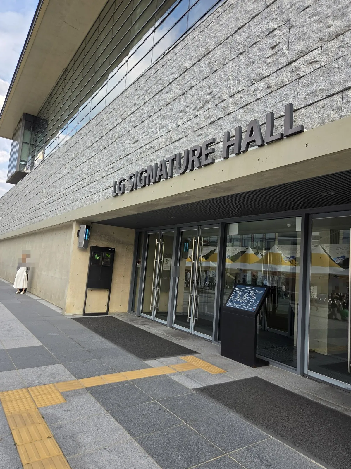 The entrance of LG SIGNATURE HALL next to the festival · the festival tents reflect in the glass
