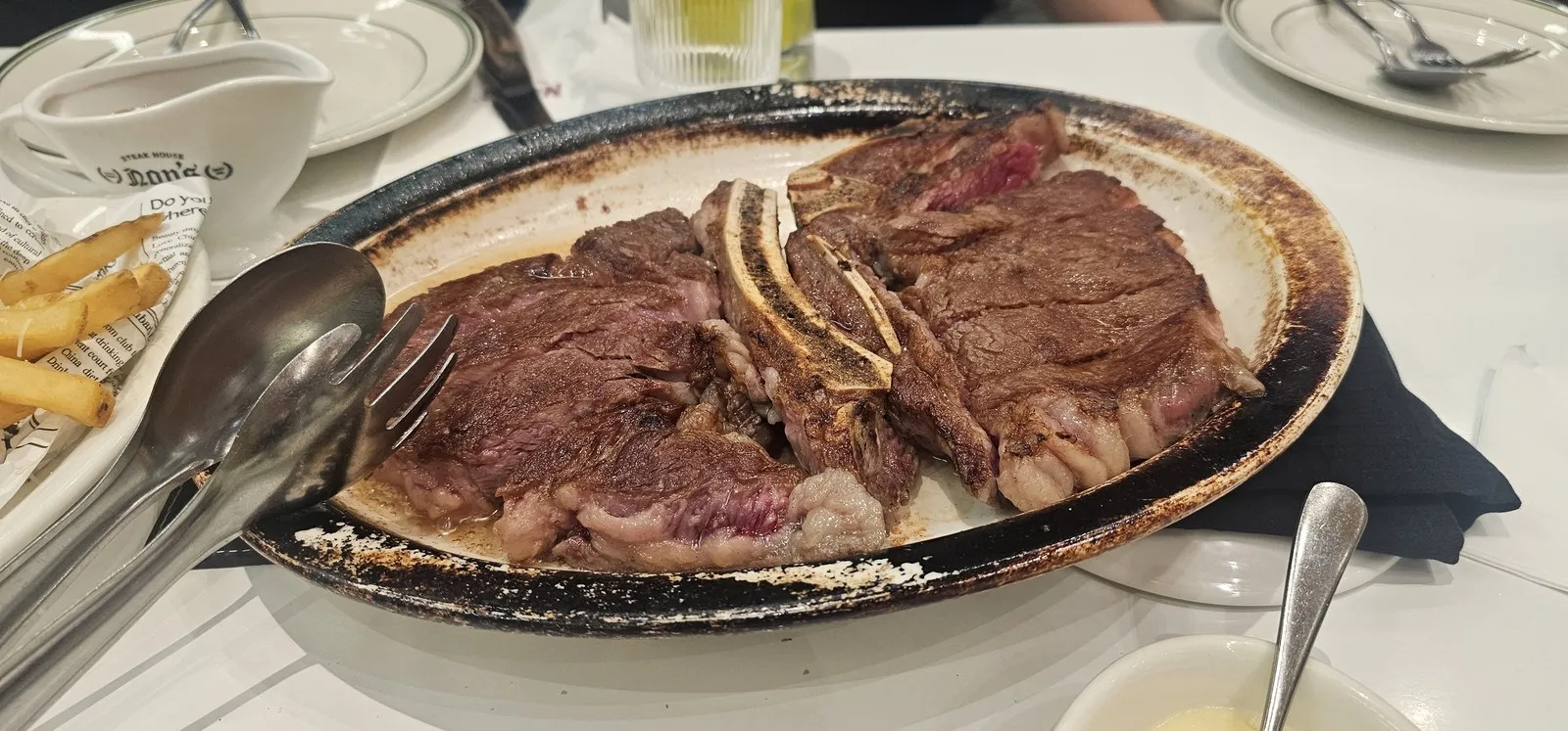 뼈째 구워 잘라 나온 스테이크 — 무쇠 오벌 접시에 그레이비 소스는 따로