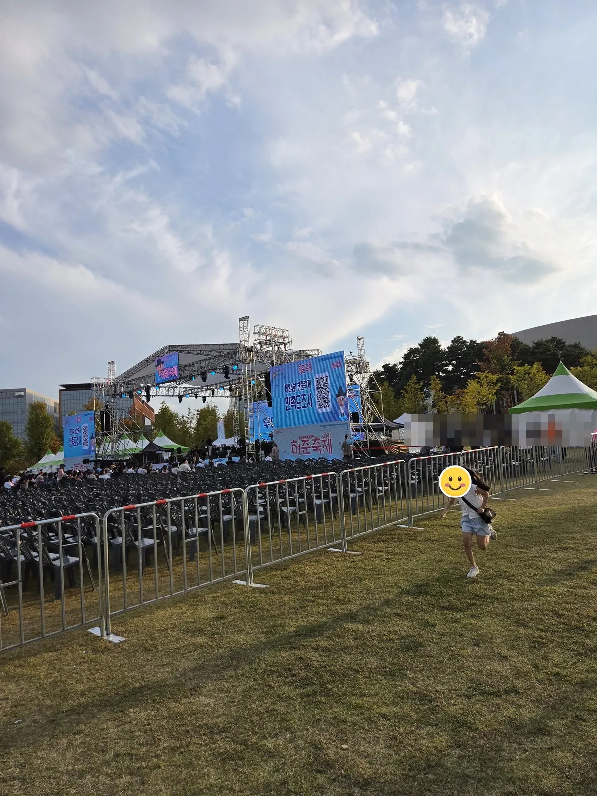 A child running across the lawn in front of the stage · the screen shows the "24th Heo Jun Festival satisfaction survey" QR code