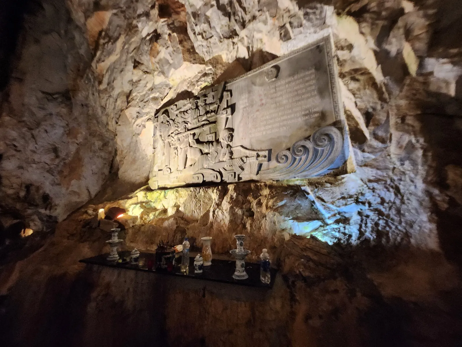 A relief stone slab on the cave wall, with an altar below (10:23)