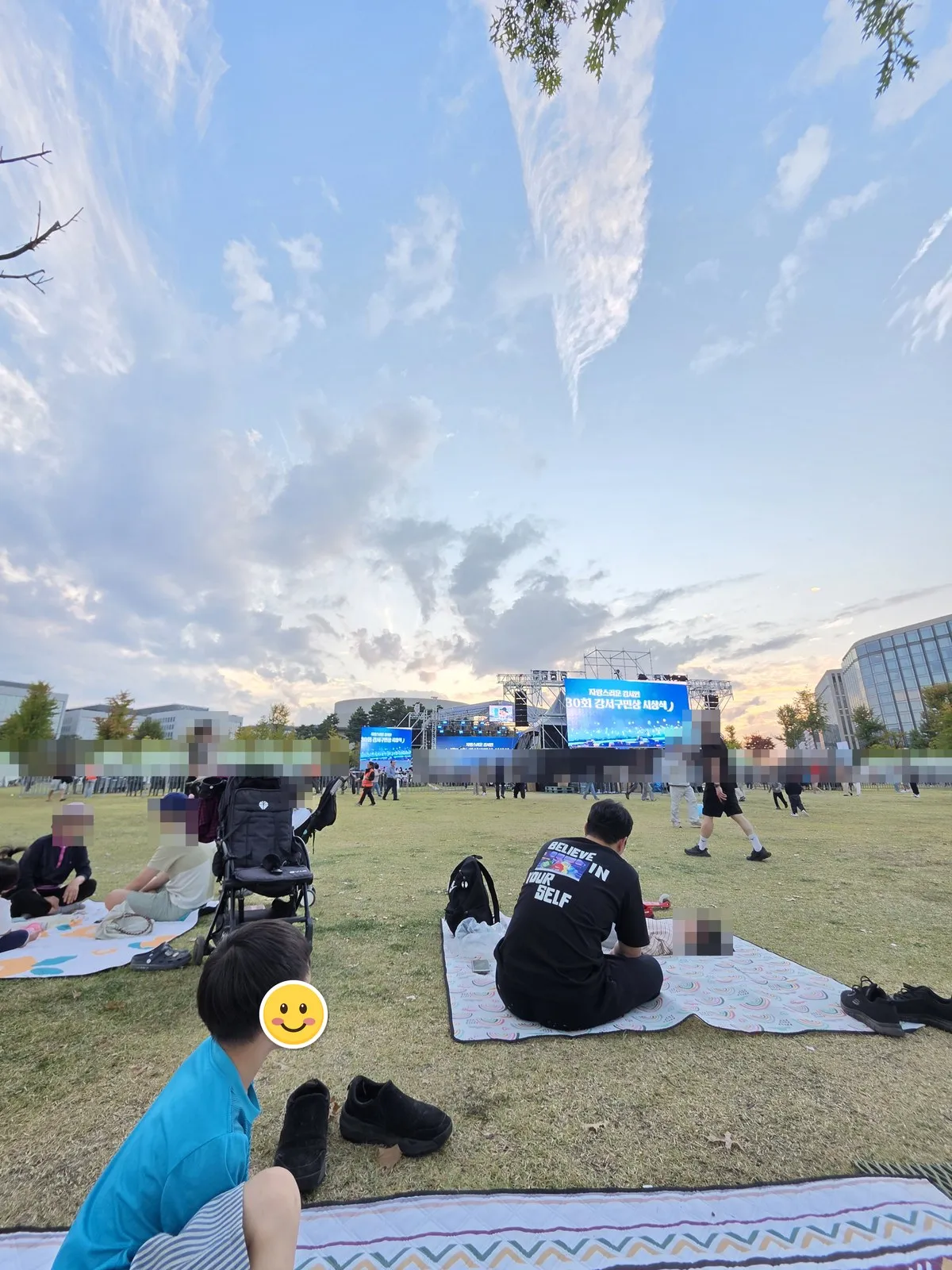 A picnic mat spread on the lawn · the stage screen reads "Proud Gangseo Citizens, 30th Gangseo-gu Citizen Awards Ceremony"