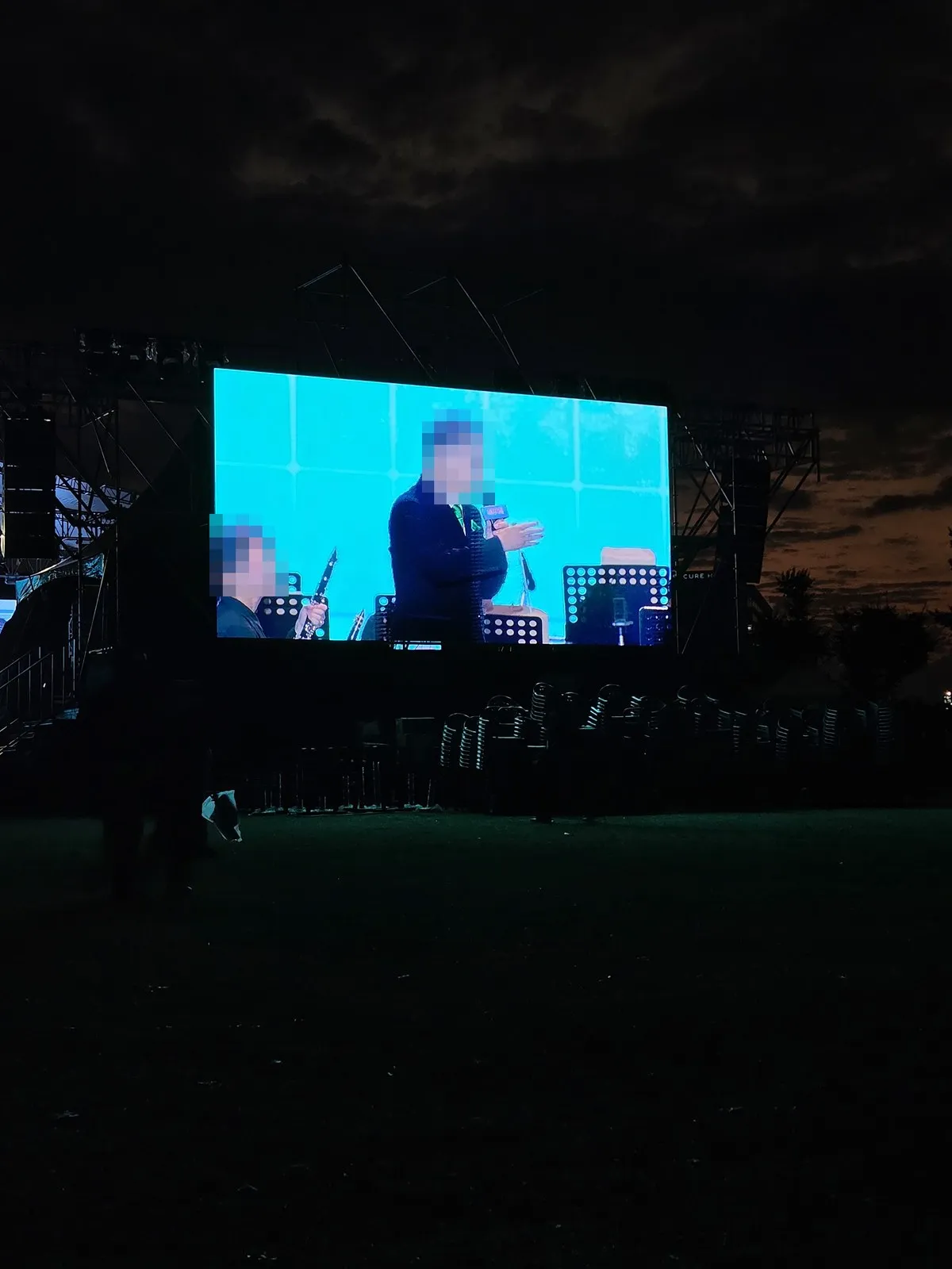 The night stage screen · a person holding a microphone and a clarinet player (faces are covered)