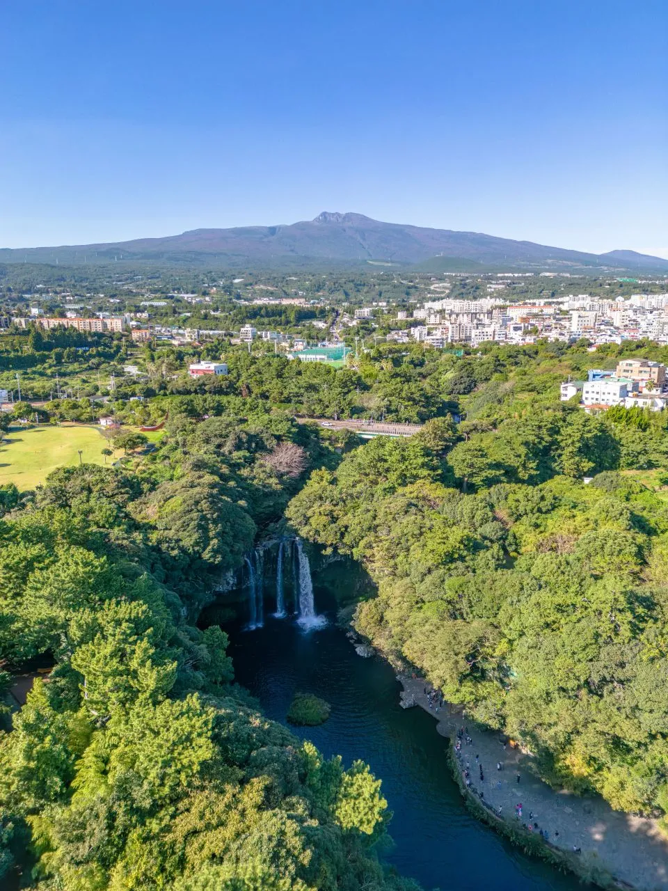 天地淵瀑布 — 以漢拏山與市區為背景的天地淵瀑布（2023年10月）（照片：韓國觀光公社觀光照片庫・攝影 황성훈・公共授權第1類）