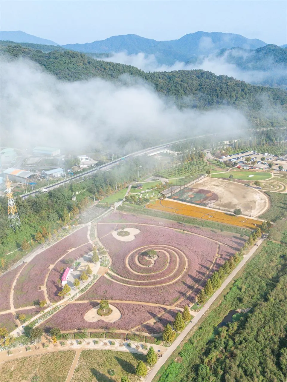 新昭陽體育公園 — 霧氣繚繞的山巒與粉黛亂子草公園空拍全景（2025年10月）