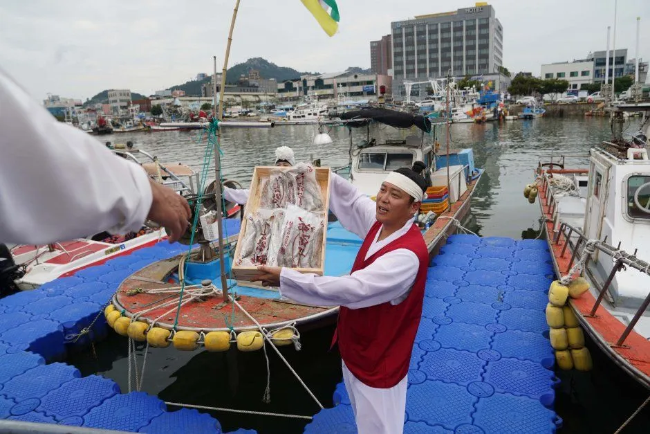 往屆慶典 — 在漁船間的浮動碼頭上高舉魚箱的表演者（照片：韓國觀光公社・公共授權第3類）